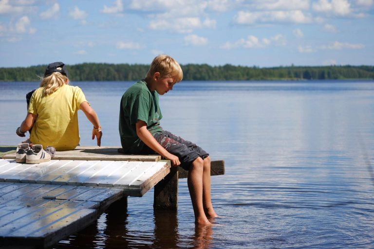 finland kids sitting on jetty by lake in summer istk