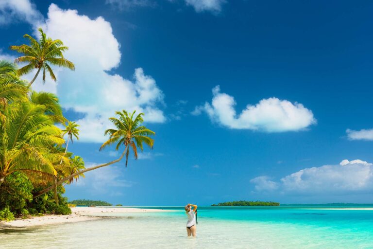 cook islands standing in crystal clear shallows on white sand beach istk