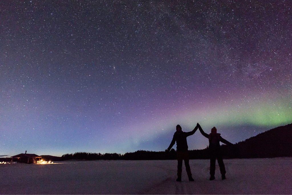 Picture of the silhouette of two people in front of the northern lights