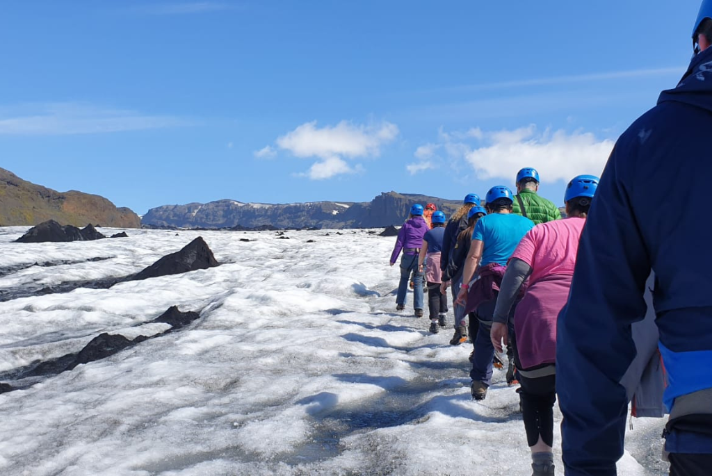 Picture of a group of people hiking on Solheimajokull snowy glacier with mountains in the background
