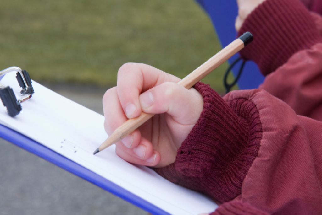 Picture of student writing on a piece of paper on a clipboard